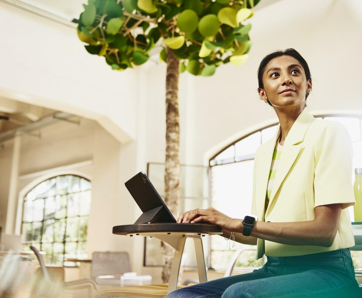 Woman looking away while sitting at table working on a tablet.