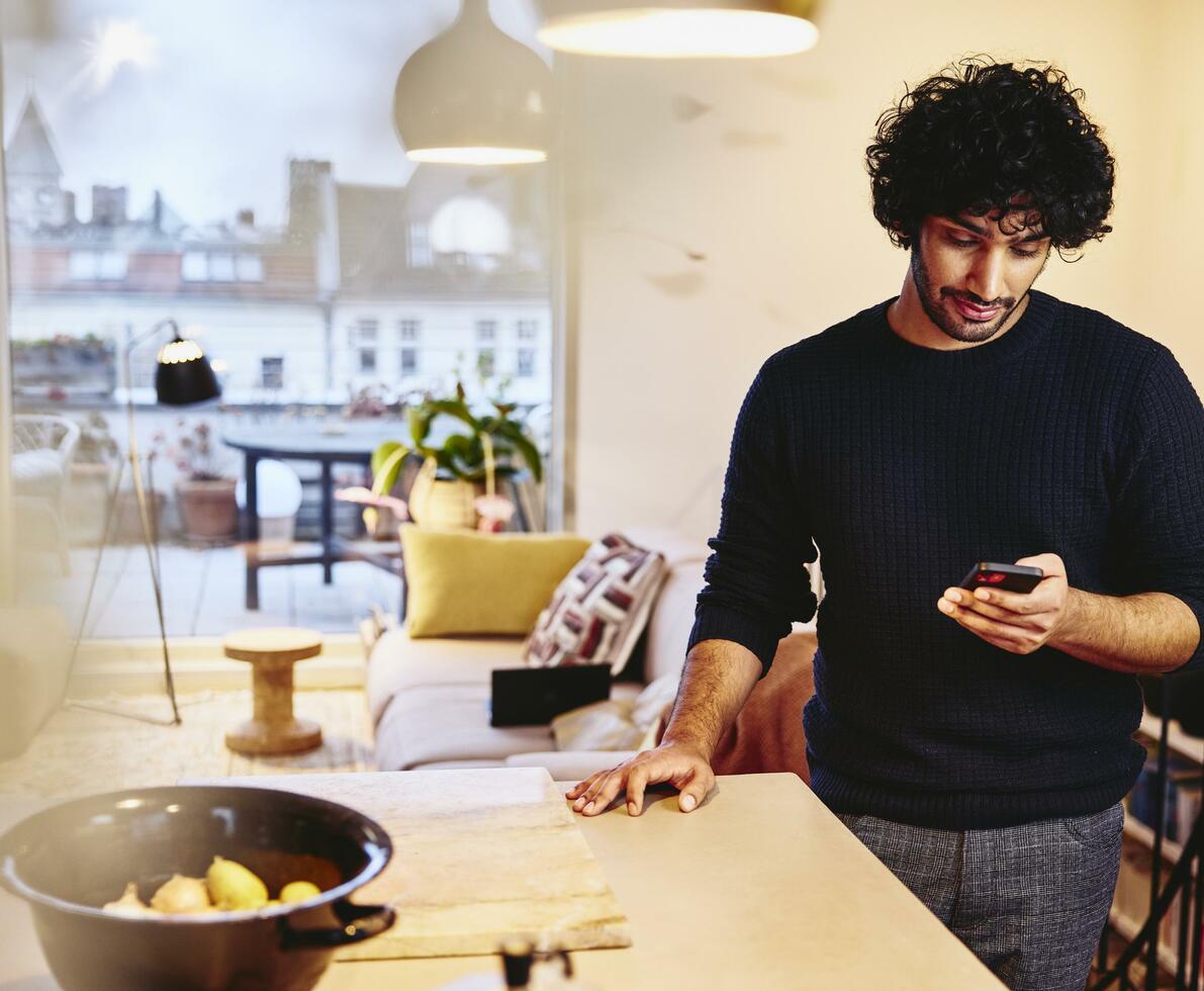 Man standing next to the kitchen counter top, looking at his phone.