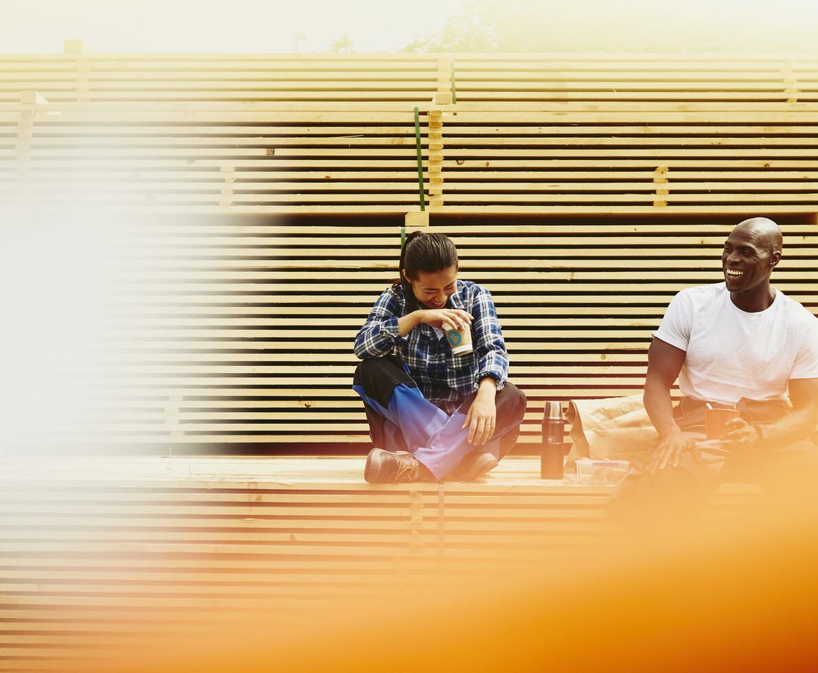 Blue-collor workers during lunch break. Laughing. Female Asian and male African-American. Checkered shirt and white T-shirt. Primary color yellow/orange. Secondary color white.