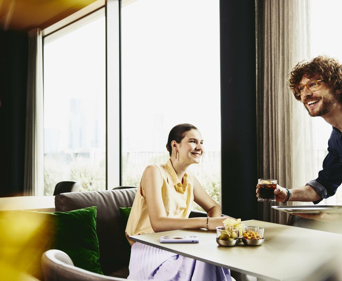 Waiter serving a drink to woman sitting at a table.