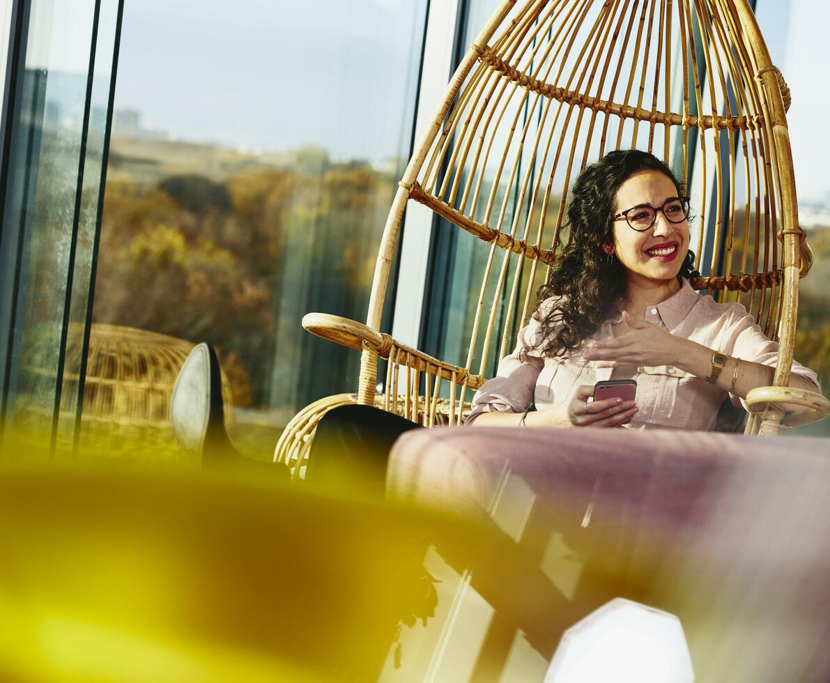 Woman smiling looking away while sitting down and holding her phone.