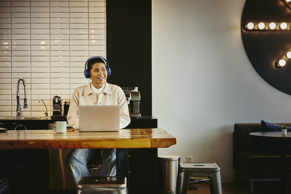 Man with headphones working on laptop at a table in a cafe